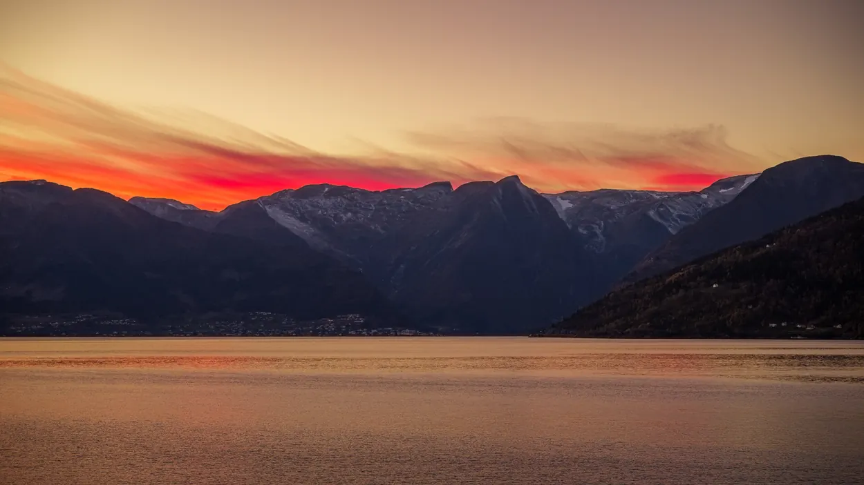 Glowing red and gold sunset over a fjord framed by dark mountain peaks